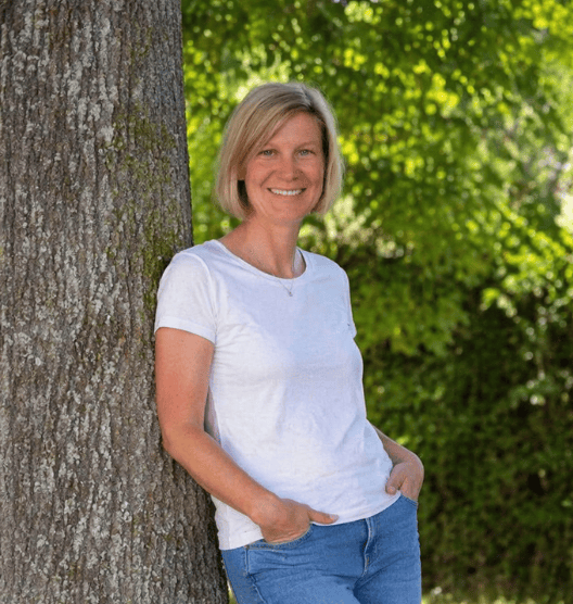 Laurence Fattebene, Life Coach in Luxemburg, lehnt entspannt an einem Baum.